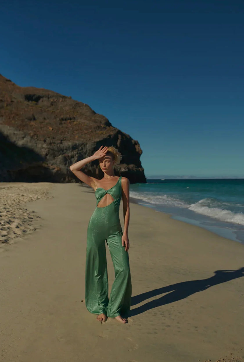 Model wearing the black Arrecife Jumpsuit, featuring a twisted halter neckline and wide-leg silhouette.