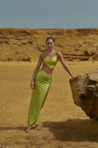 Model wearing the Grasshopper-colored Cala Set, featuring a one-shoulder top with wraparound tie and a midi-length skirt with side slit.