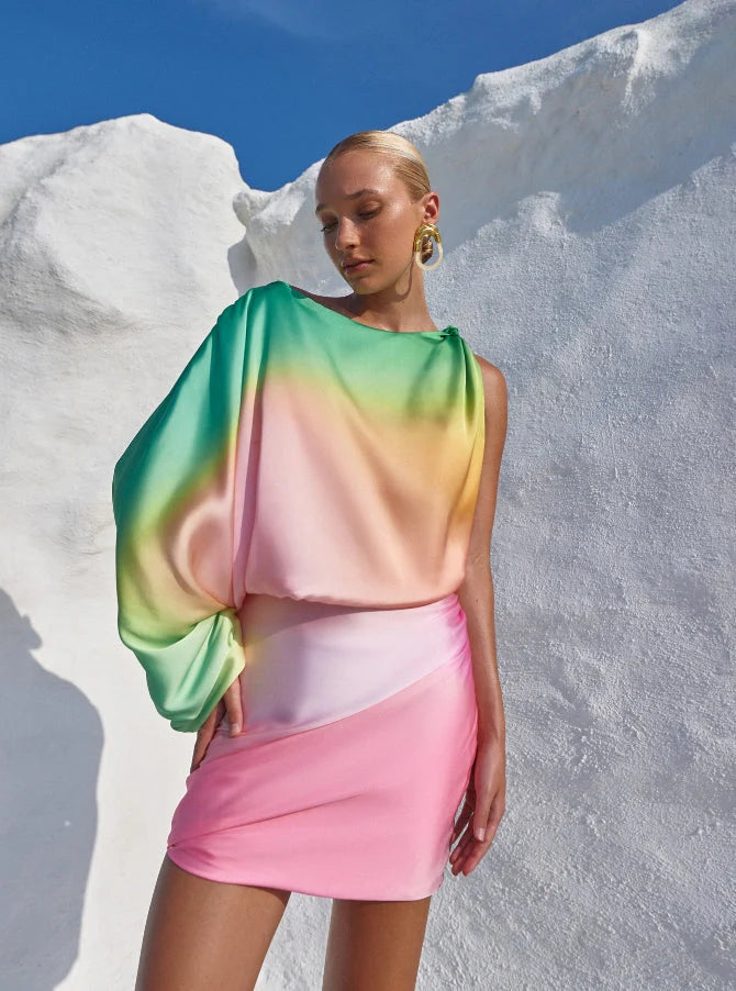 Model posing outdoors in the Dolly Dress, showing its asymmetric silhouette and vibrant pastel palette.