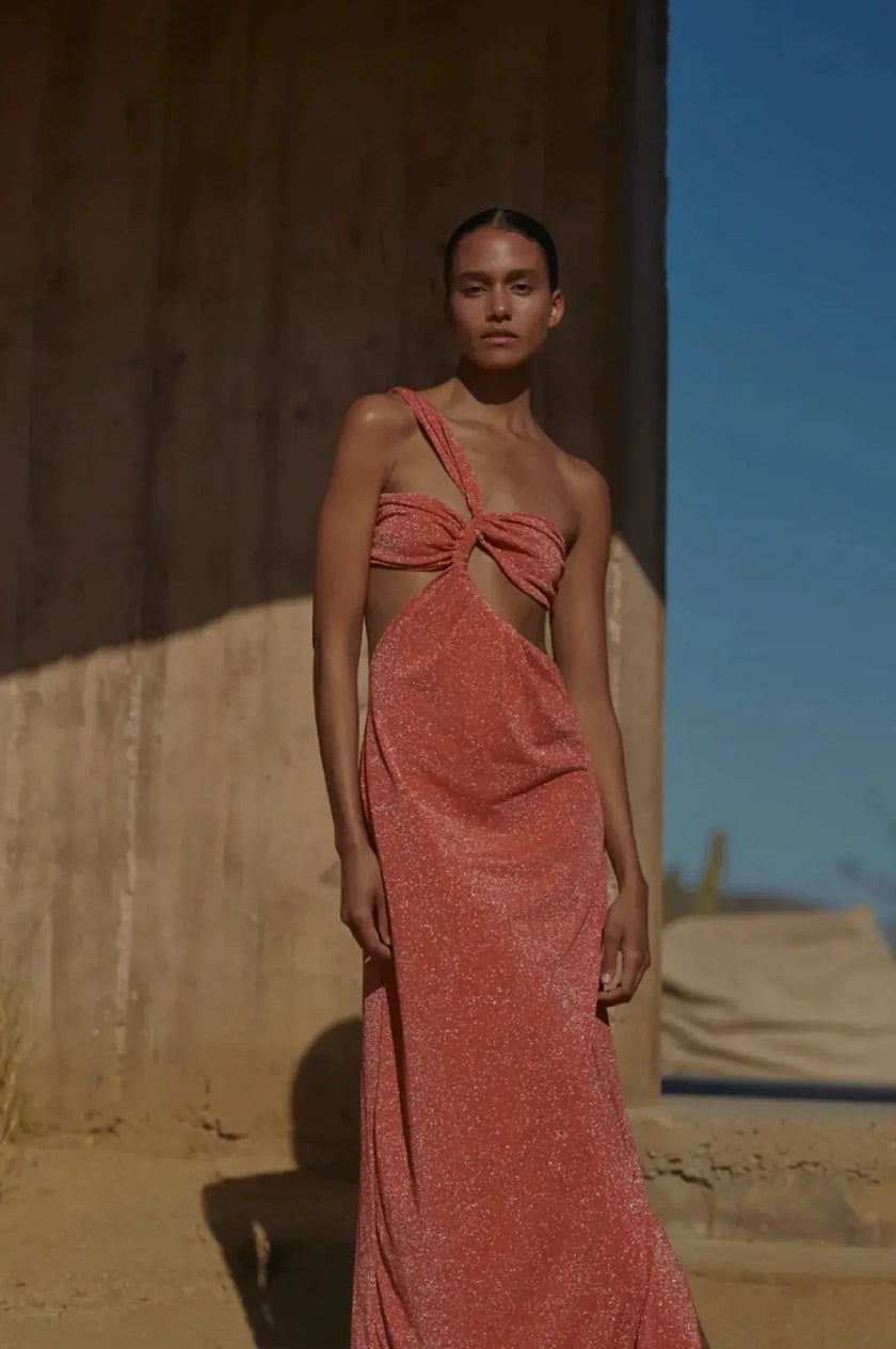 Model wearing the Rosatua-colored Noah Dress, showcasing its one-shoulder design with asymmetric cutouts and a twisted top detail.