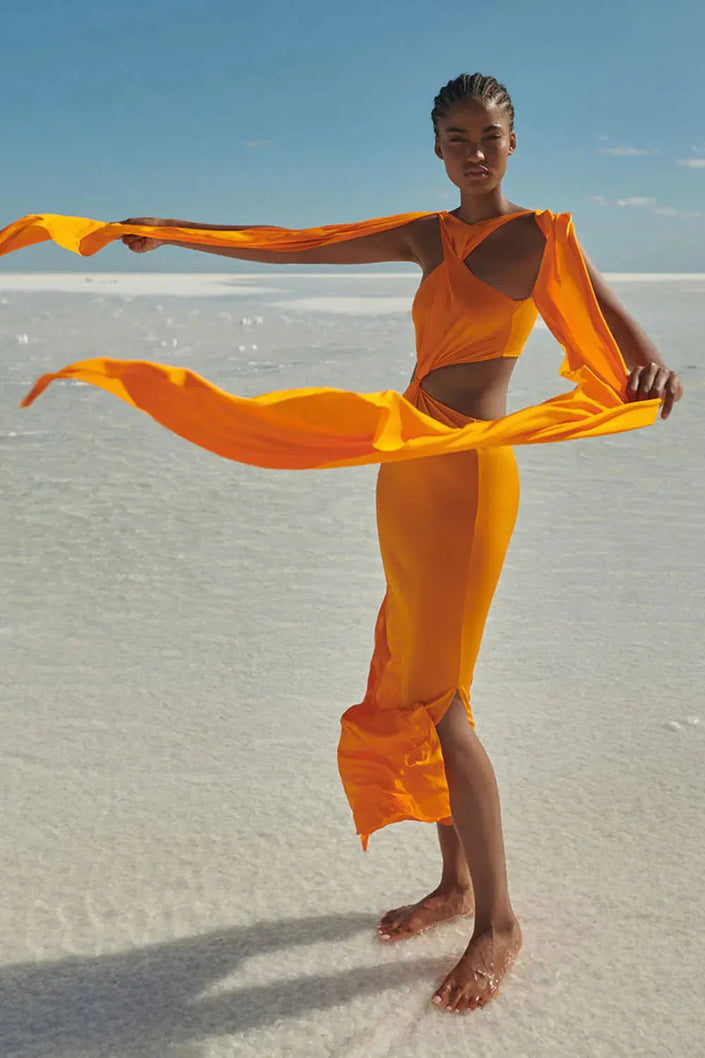 Model wearing the Ribera Maxi Dress in Amber, showcasing its halter neckline, side cutouts, and thigh-high slit.