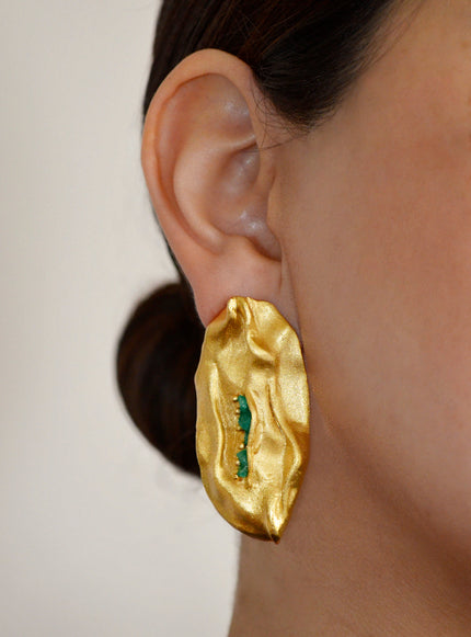 Close-up of the Bimy Emerald Earring worn by a model, showcasing its organic gold shape and vibrant Colombian emeralds.