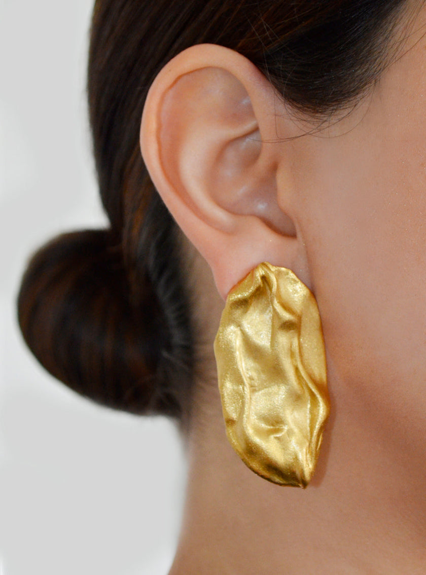 Close-up of the Bimy earring worn by a model, highlighting its sculptural gold form and textured finish.