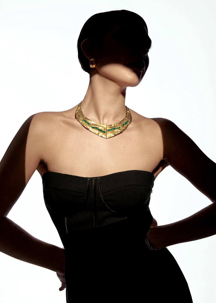 Model wearing the Bimy necklace with a strapless black dress, highlighting the textured gold and green stones under dramatic lighting.