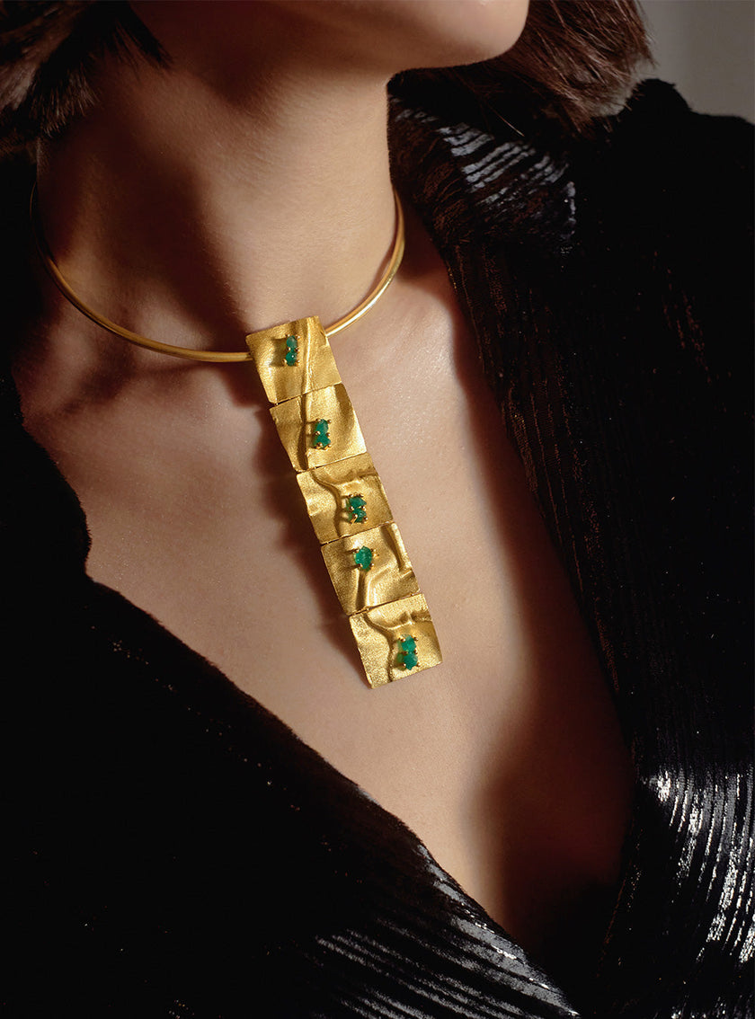 Model wearing the Moky necklace with a black textured dress, showcasing its sculptural pendant with emeralds.