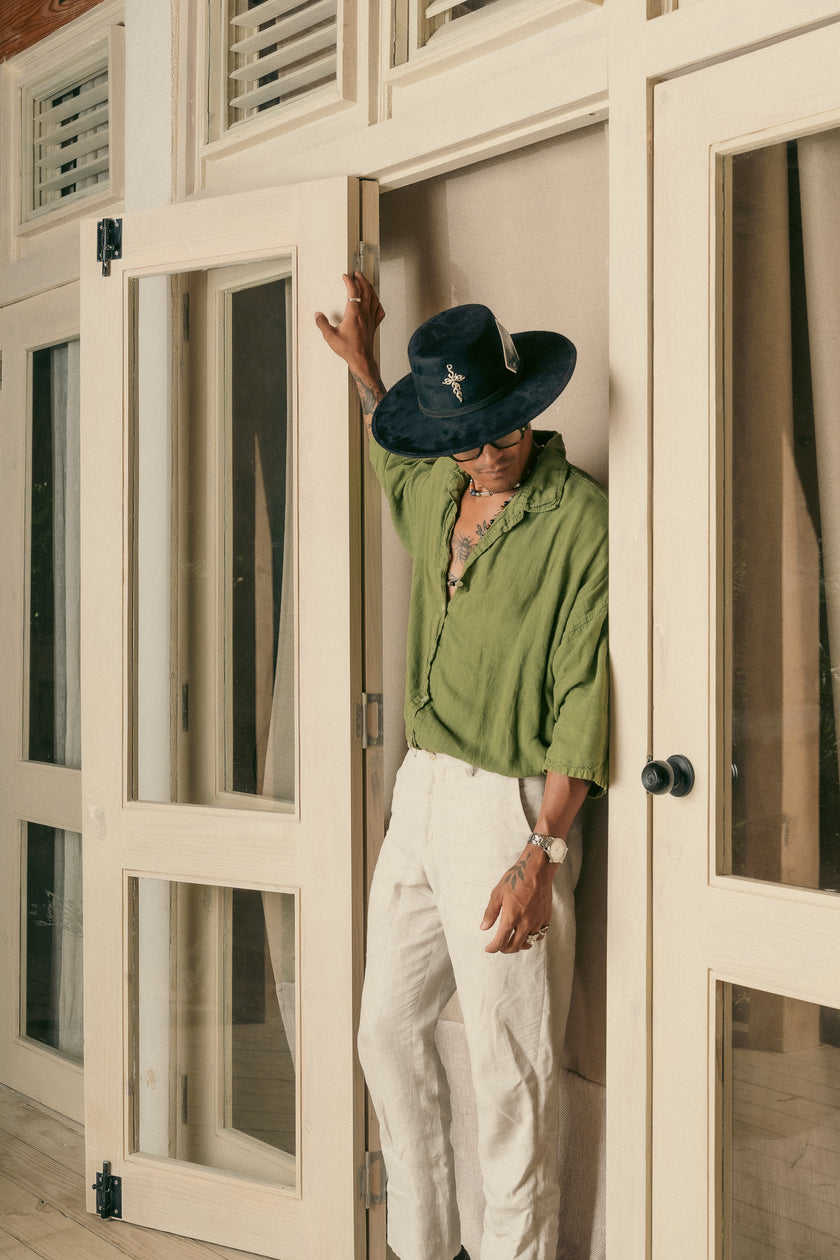 Side view of a man in a black Cross Charm hat with card detail, dressed in white pants and green shirt.