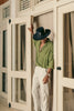 Side view of a man in a black Cross Charm hat with card detail, dressed in white pants and green shirt.