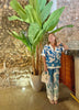 Model wearing the Eloisa Long Set by ANTIBES in Punta Cana, featuring a silky, tropical-print ensemble in shades of blue and green, styled with nude heels and a confident pose under moody lighting.