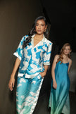 Model walking confidently down a hallway in Punta Cana wearing the Eloisa Long Set by ANTIBES, with a second model in a turquoise silk slip dress in the background, creating a contrast of textures and tones.