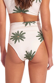 Woman wearing a white bikini with palm tree patterns on a plain background