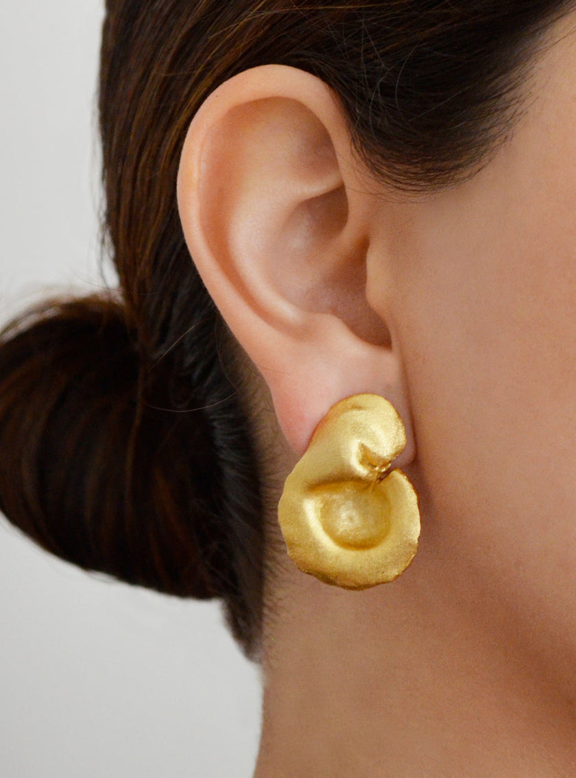 Close-up of a model wearing a sculptural gold earring with an abstract organic shape.