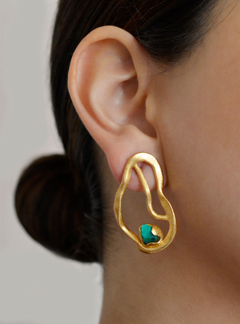 Close-up of the Fuswa earring worn by a model, featuring an abstract gold shape with a raw Colombian emerald.