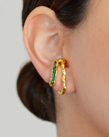 Close-up of a woman's ear adorned with a sculptural double hoop earring in gold with raw emeralds.