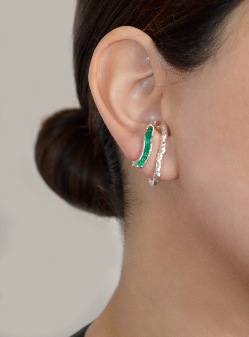 Side view of a silver and emerald double hoop earring worn on a woman with her hair in a low bun.