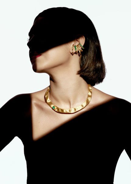 Model wearing the Guity Emerald Choker with layered gold earrings, styled with dramatic light and shadow.