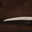 Close-up of cream hand-carved tooth detail wrapped in thread, attached to dark brown luxury felt hat.