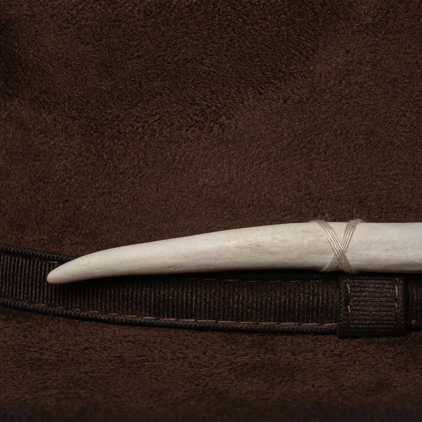 Close-up of cream hand-carved tooth detail wrapped in thread, attached to dark brown luxury felt hat.