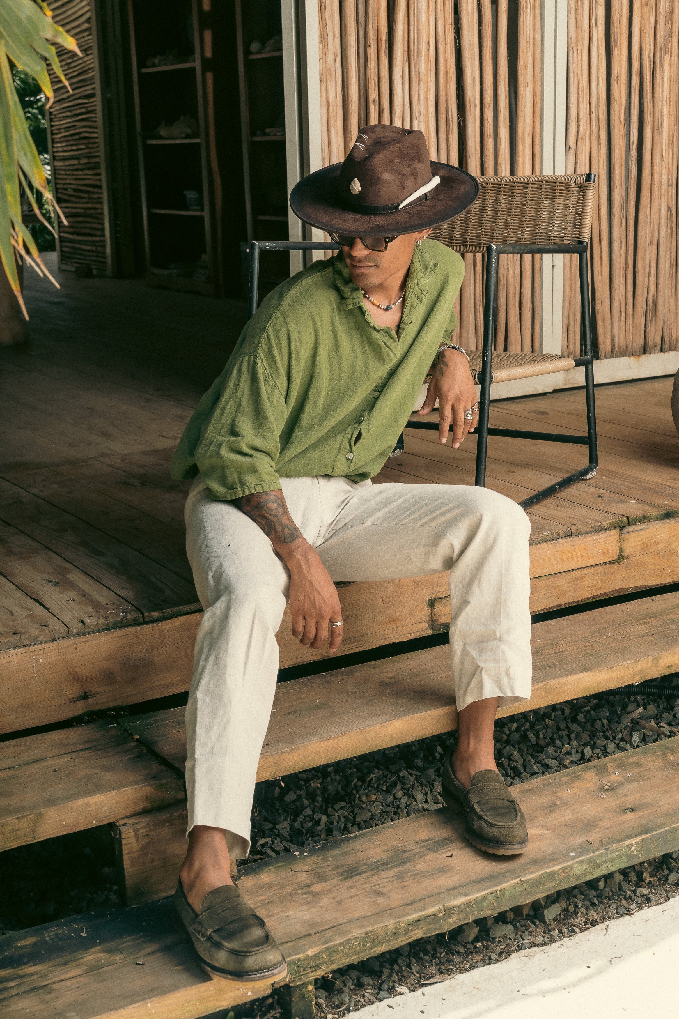 Model wearing Hunter hat by Mamba Hats while sitting on rustic wooden stairs, surrounded by Caribbean decor