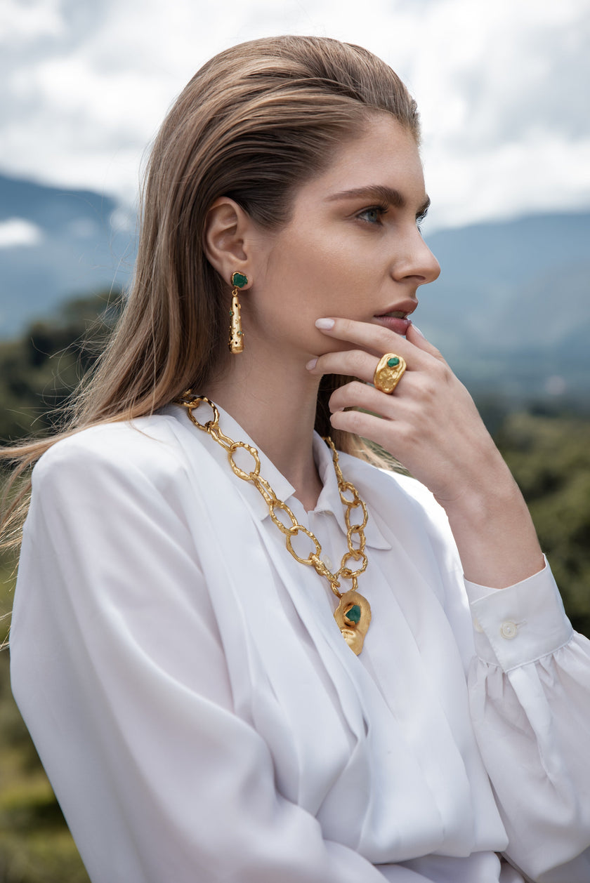 Editorial shot of a model wearing the Hyba ring, paired with matching emerald jewelry, in an outdoor setting with natural light.
