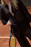 Street-style moment in Punta Cana featuring a woman wearing the MAUI Long Set by ANTIBES — a sheer black outfit paired with a quilted handbag and sunglasses, blending urban chic with tropical sophistication.
