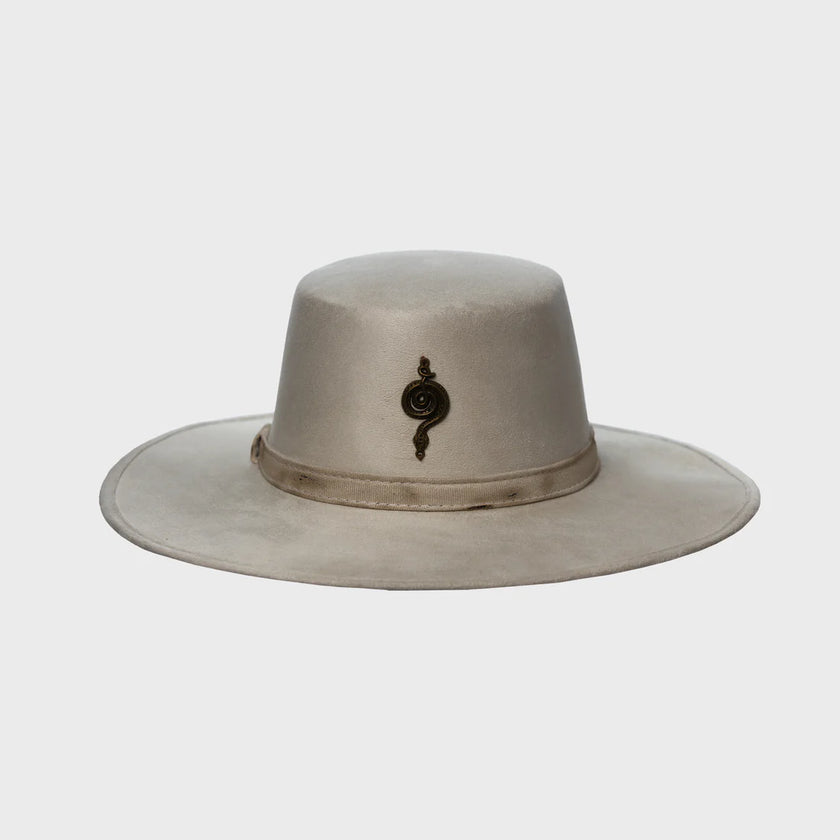Front-facing close-up of the Mamba Charm wide-brim hat in light sand color, featuring a metallic snake-inspired emblem, set against a clean white background.