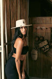 Woman with long black hair wearing the Mamba Charm hat in a tropical rustic interior, paired with a sleek black outfit that highlights the artisanal design.