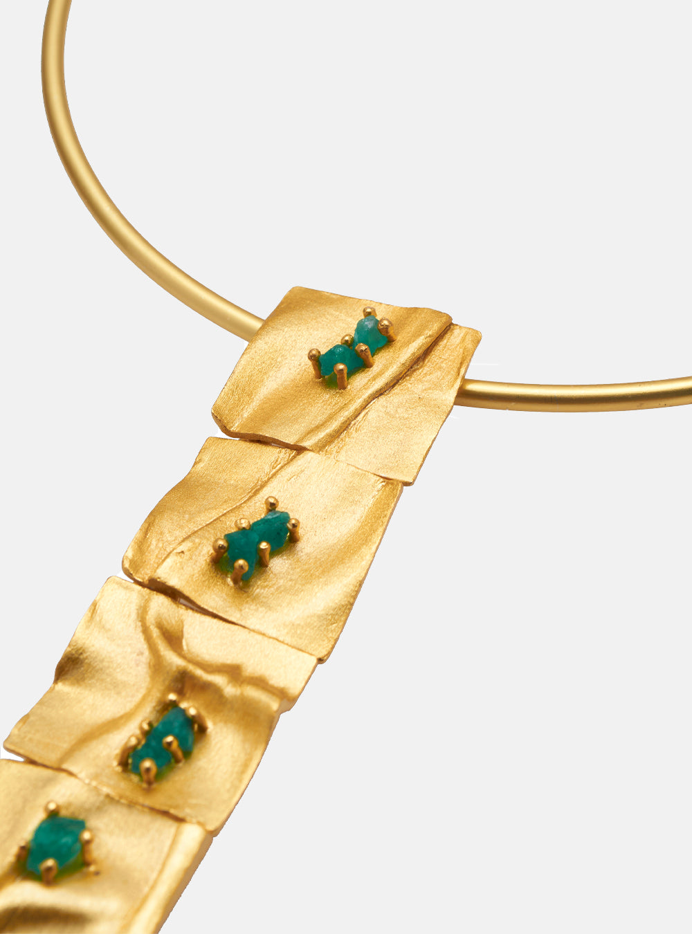 Close-up of the Moky necklace pendant, highlighting its gold texture and vibrant emerald settings.