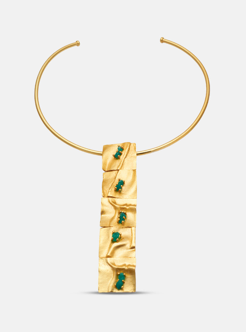 Frontal view of the Moky necklace against a white background, featuring a bold pendant with emerald-set gold plates.