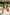 Woman with tattoos wearing the Olive Pirates hat and beige linen dress, under a palm-thatched roof near a tropical pool.