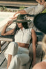 Model lounging on a wooden poolside deck chair, wearing the Olive Pirates hat with white linen outfit, evoking effortless summer elegance.