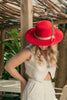 op-down view of woman in neutral linen outfit and red hat with feather, captured in a quiet tropical setting under filtered sunlight.